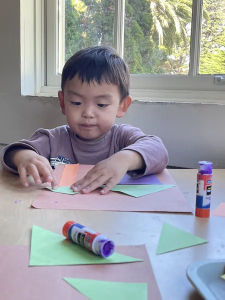 Everest at the table, gluing green paper triangles onto pink paper