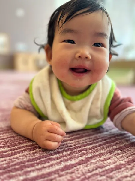 Maggie grinning on the rug in a green-trimmed bib